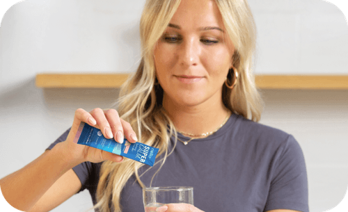 Person pouring supplement powder into a glass of water.