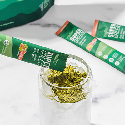 Single-serve packet of green powder being poured into a glass with more packets in the background.